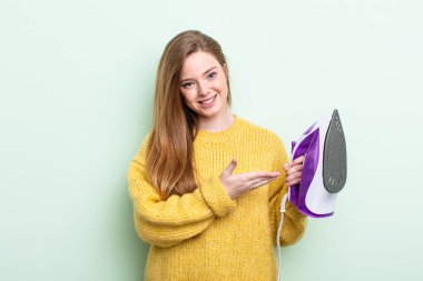 Kızıl saçlı kadın neşeyle gülümsüyor, mutlu hissediyor ve bir konsept gösteriyor. Demir giysi konsepti