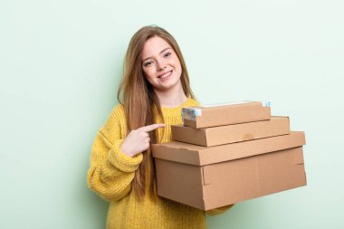 Kızıl saçlı kadın neşeyle gülümsüyor, mutlu hissediyor ve bir tarafı işaret ediyor. paket kutuları konsepti