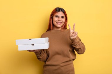 İspanyol kadın gülümsüyor ve arkadaş canlısı görünüyor, iki numarayı gösteriyor. Pizza konseptini kaldır.