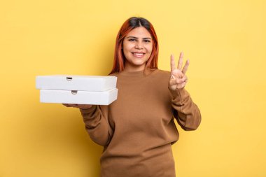 İspanyol kadın gülümsüyor ve arkadaş canlısı görünüyor, üç numarayı gösteriyor. Pizza konseptini kaldır.