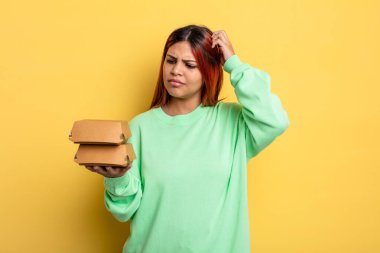 İspanyol kadın mutlu bir şekilde gülümsüyor ve hayal kuruyor ya da şüphe ediyor. Hamburger konseptini kaldır.