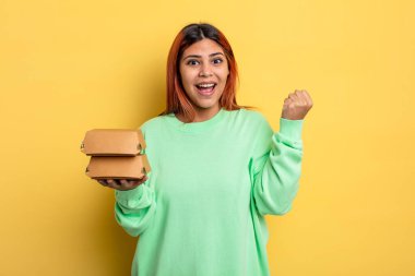 İspanyol kadın şokta, gülüyor ve başarıyı kutluyor. Hamburger konseptini kaldır.