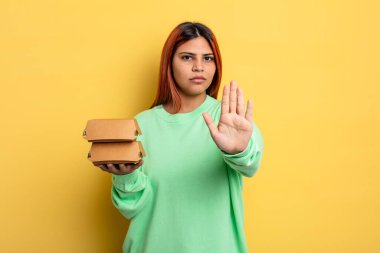 İspanyol kadın ciddi görünüyor. Avuç içini gösteriyor. Durdurma hareketi yapıyor. Hamburger konseptini kaldır.