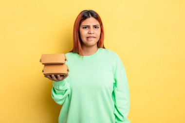 İspanyol kadın şaşkın ve şaşkın görünüyor. Hamburger konseptini kaldır.