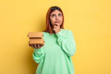 Hispanik kadın düşünüyor, kuşkulu ve şaşkın hissediyor. Hamburger konseptini kaldır.