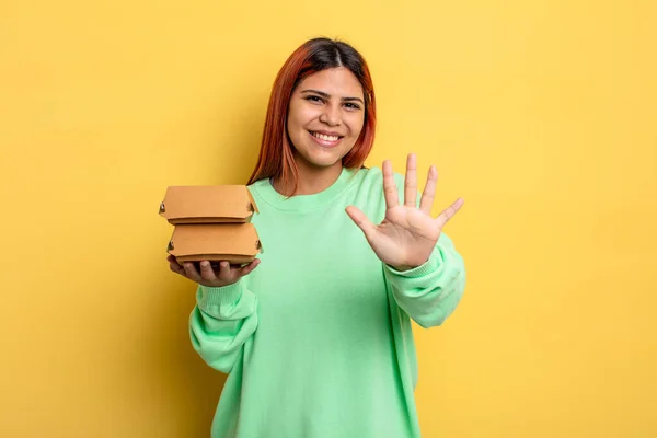 ヒスパニック系の女性は笑顔で友好的に見える5番目を示しています ハンバーガーの概念を取り上げ — ストック写真