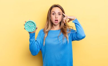 pretty woman looking surprised, realizing a new thought, idea or concept holding an alarm clock