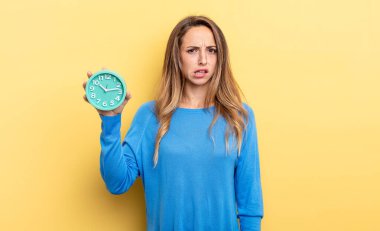 pretty woman feeling puzzled and confused holding an alarm clock