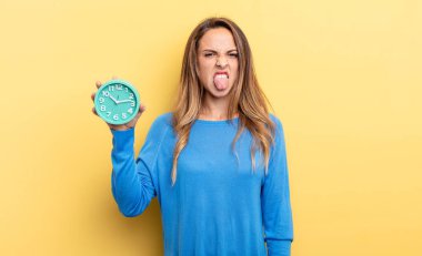 pretty woman feeling disgusted and irritated and tongue out holding an alarm clock