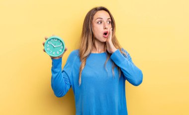 pretty woman feeling happy, excited and surprised holding an alarm clock