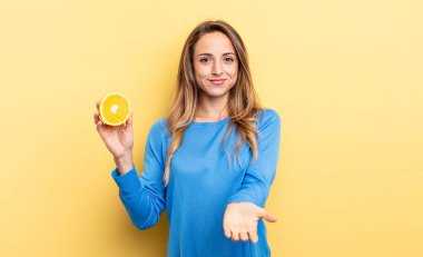 pretty woman smiling happily with friendly and  offering and showing a concept holding half orange