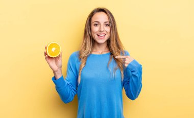 pretty woman feeling happy and pointing to self with an excited holding half orange