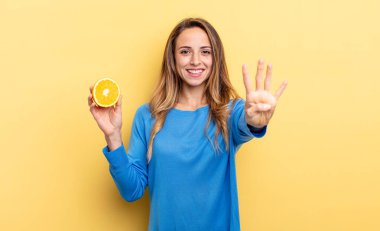 pretty woman smiling and looking friendly, showing number four holding half orange