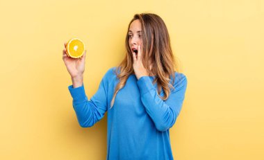pretty woman feeling happy, excited and surprised holding half orange