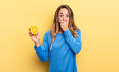 pretty woman covering mouth with hands with a shocked holding half orange