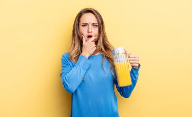 pretty woman with mouth and eyes wide open and hand on chin orange juice concept