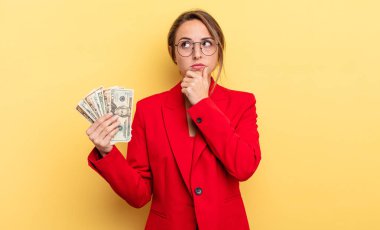 pretty woman thinking, feeling doubtful and confused. business and dollar banknotes concept