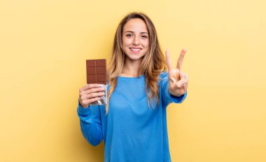 pretty woman smiling and looking friendly, showing number two. chocolate concept