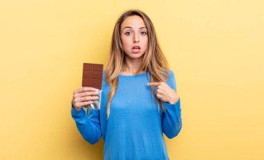 pretty woman looking shocked and surprised with mouth wide open, pointing to self. chocolate concept