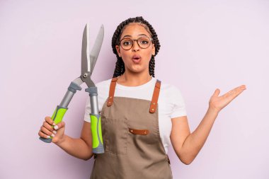 Siyah afro kadın şaşırmış ve şok olmuş görünüyor. Çenesi düşmüş ve elinde bir nesne tutuyor. Bahçıvan ya da çiftçi konsepti
