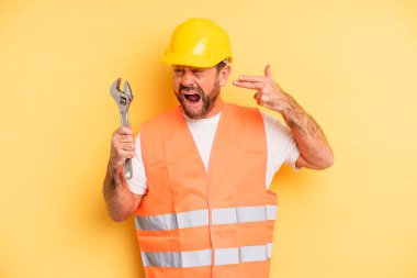middle age man looking unhappy and stressed, suicide gesture making gun sign.  breakdown car repair wrench concept