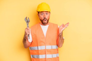 middle age man looking surprised and shocked, with jaw dropped holding an object.  breakdown car repair wrench concept
