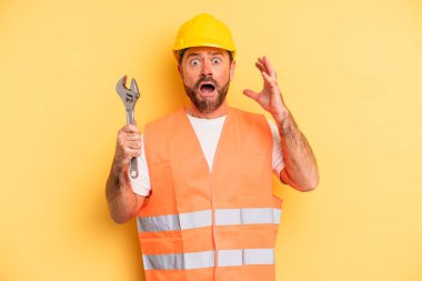 middle age man screaming with hands up in the air.  breakdown car repair wrench concept
