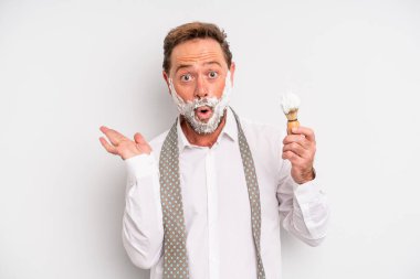 Orta yaşlı bir adam şaşırmış ve şok olmuş görünüyor. Çenesi düşmüş ve elinde bir nesne var. Tıraş fırçası ve köpük kavramı