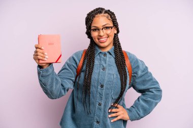 Siyah afro kadın mutlu bir şekilde gülümsüyor, eli kalçasında ve kendinden emin. Öğrenci takvimi veya ajanda kavramı