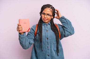 Siyah afro kadın mutlu bir şekilde gülümsüyor ve hayal kuruyor ya da şüphe ediyor. Öğrenci takvimi veya ajanda kavramı