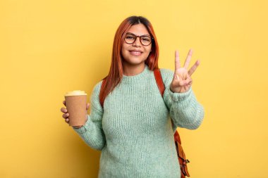 İspanyol kadın gülümsüyor ve arkadaş canlısı görünüyor, üç numarayı gösteriyor. Kahve konsepti olan bir öğrenci