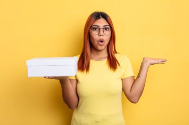 İspanyol kadın şaşırmış ve şok olmuş görünüyor. Çenesi düşmüş ve elinde bir nesne tutuyor. boş ambalaj kavramı