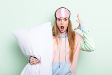 Kızıl saçlı kadın ellerini havaya kaldırarak çığlık atıyor. Pijama ve yastık konsepti