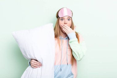 Kızıl saçlı kadın şok olmuş bir şekilde ağzını eliyle kapatıyor. Pijama ve yastık konsepti
