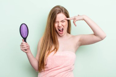 Kızıl saçlı kadın mutsuz ve stresli görünüyor, intihar jesti silah işareti yapıyor. saç tarağı konsepti