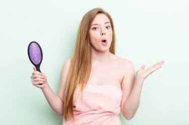 Kızıl saçlı kadın şaşırmış ve şok olmuş görünüyor. Çenesi düşmüş ve elinde bir nesne var. saç tarağı konsepti