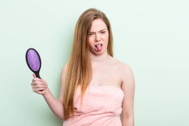 Kızıl saçlı kadın iğreniyor, sinirleniyor ve dili dışarı çıkıyor. saç tarağı konsepti