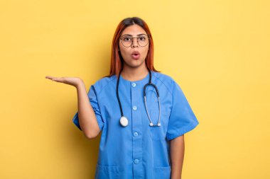 İspanyol kadın şaşırmış ve şok olmuş görünüyor. Çenesi düşmüş ve elinde bir nesne tutuyor. hemşire konsepti