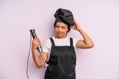 afro black woman feeling puzzled and confused, scratching head. chef with hand blender