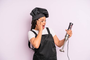 afro black woman feeling happy, excited and surprised. chef with hand blender