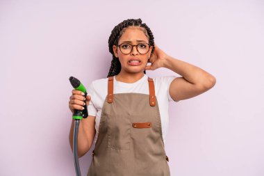 afro black woman feeling stressed, anxious or scared, with hands on head. gardener hose concept