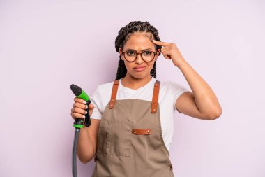 afro black woman feeling confused and puzzled, showing you are insane. gardener hose concept