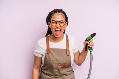 afro black woman shouting aggressively, looking very angry. gardener hose concept