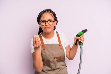 afro black woman making capice or money gesture, telling you to pay. gardener hose concept