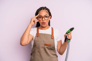 afro black woman looking surprised, realizing a new thought, idea or concept. gardener hose concept