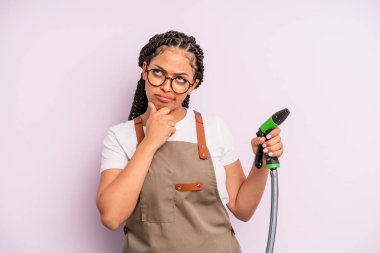 afro black woman thinking, feeling doubtful and confused. gardener hose concept