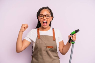 afro black woman shouting aggressively with an angry expression. gardener hose concept