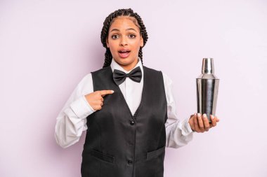afro black woman looking shocked and surprised with mouth wide open, pointing to self. waiter with a cocktail