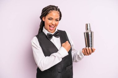 afro black woman feeling happy and facing a challenge or celebrating. waiter with a cocktail