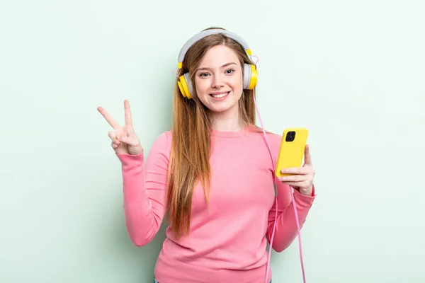 Redhair Woman Smiling Looking Friendly Showing Number Two Headphones Smartphone — Stock Photo, Image
